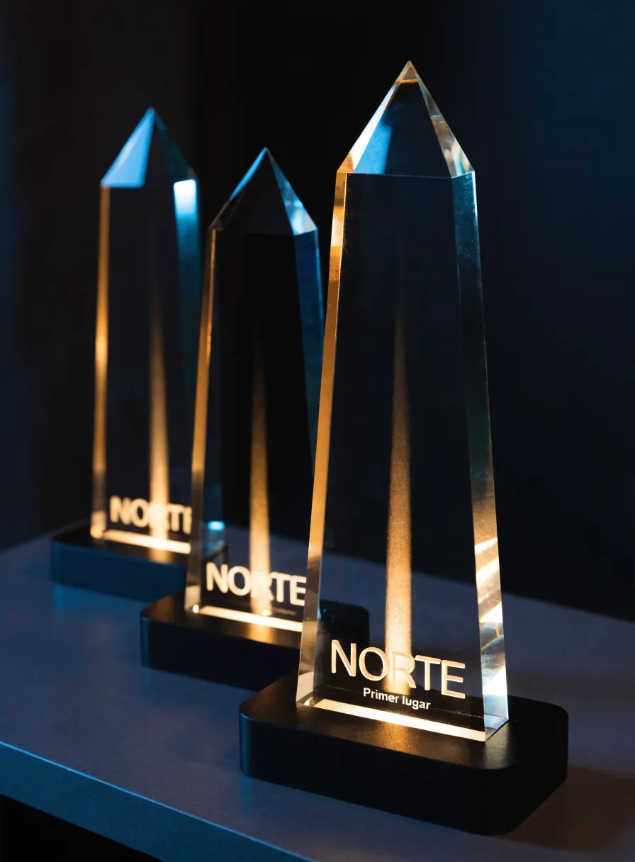 tres obeliscos de cristal de alturas distintas sobre bases negras encendidas, el de enfrente grabado con la palabra Norte y la línea Primer lugar