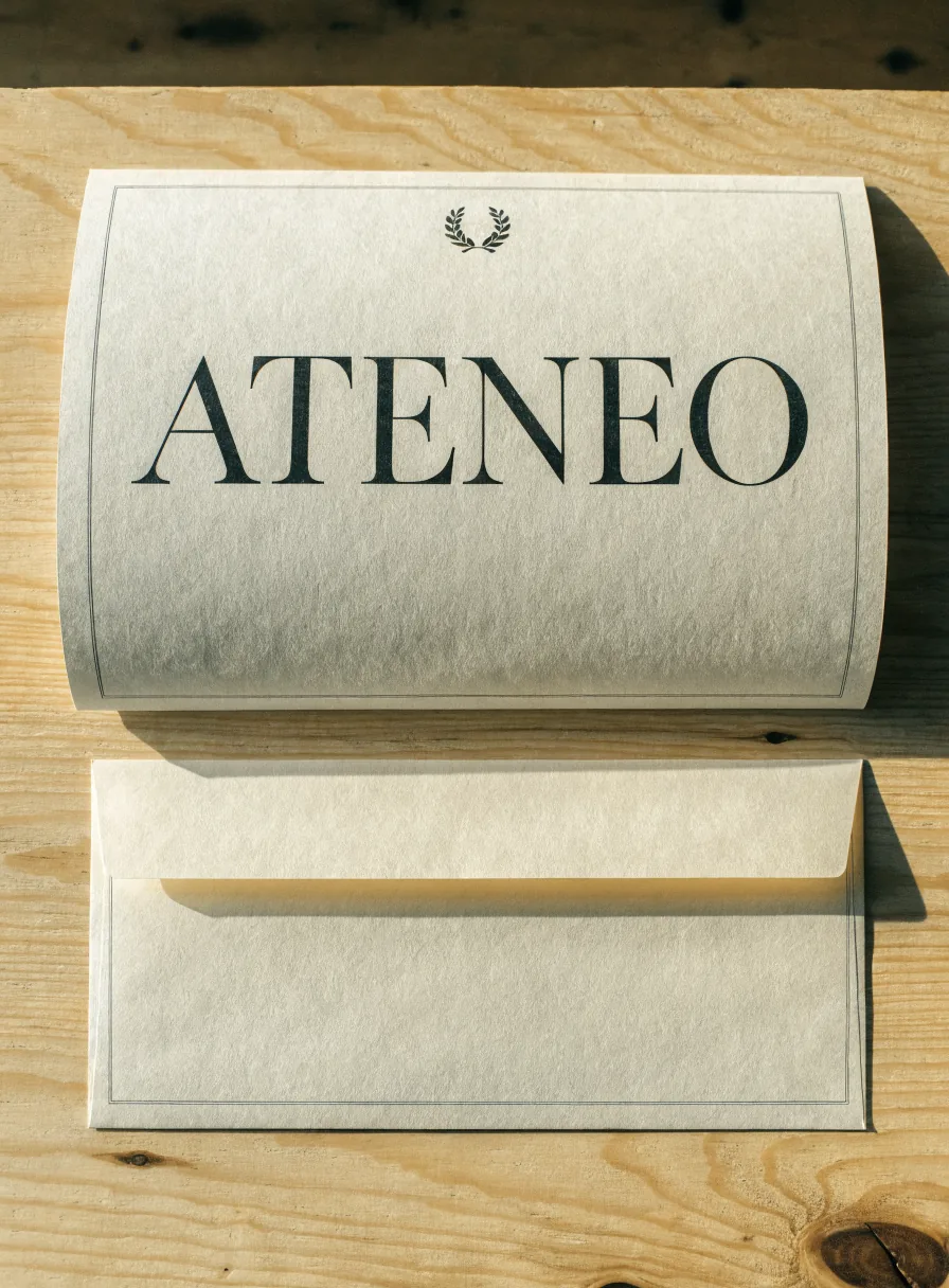 diploma impreso a dos tintas en papel marfil texturizado, extendido sobre una mesa de roble junto a su sobre de entrega hecho a la medida en el mismo papel, ambos con un filete fino impreso alrededor, una corona de laurel al centro arriba y la palabra Ateneo debajo