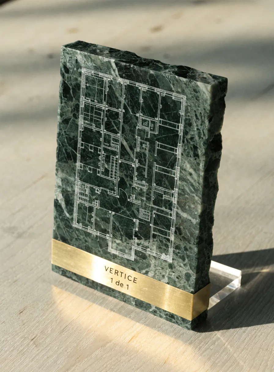 losa de mármol verde veteado con los cantos rotos a la vista, grabada a mano con el plano de una planta arquitectónica y las líneas rellenas de pigmento blanco, con una banda de latón embutida abajo grabada VERTICE y 1 de 1