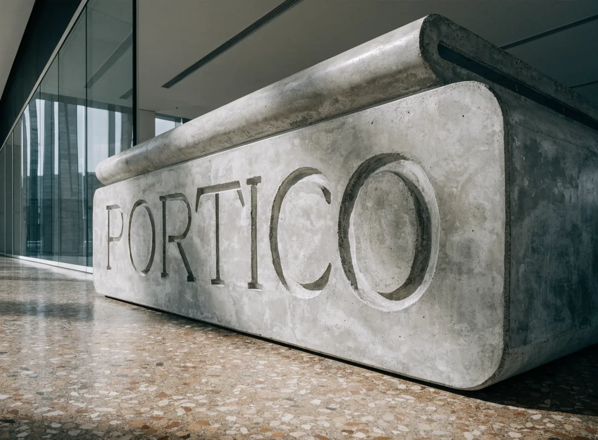 banca monolito de concreto colado con la palabra PORTICO grabada en bajorrelieve, en un vestíbulo de cristal con piso de terrazo