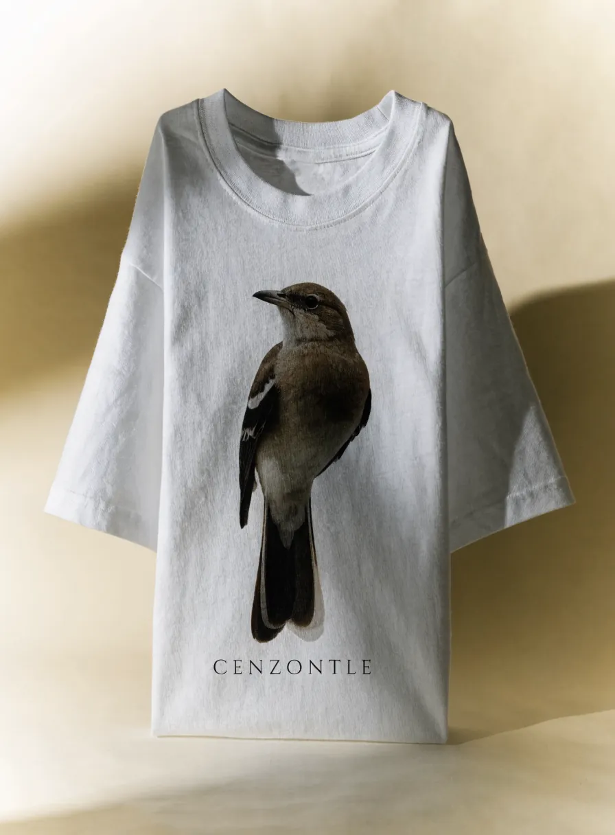 Playera blanca de algodón de cuello redondo, vista de frente, con un cenzontle impreso a todo color y la palabra CENZONTLE en letras espaciadas debajo.
